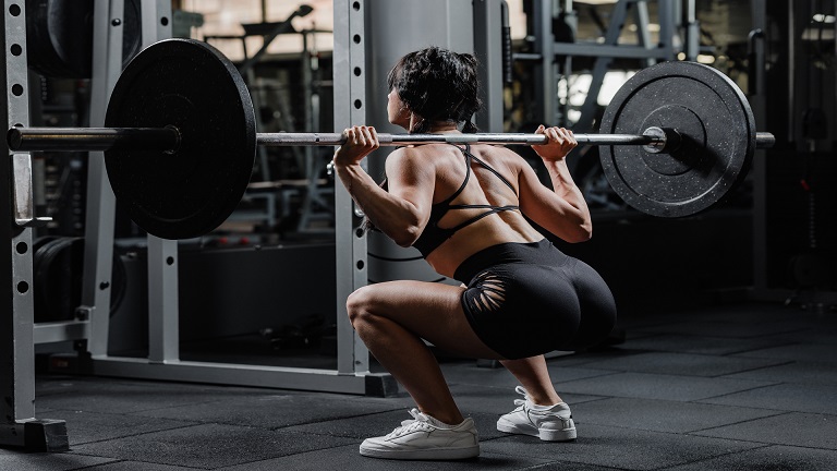 Muscular lifter performing a barbell back squat showing start and bottom positions