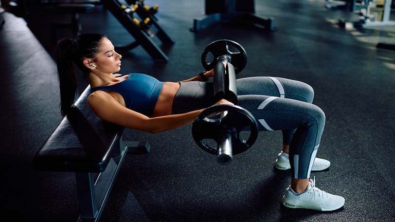 Lifter performing a barbell hip thrust at full lockout in a gym setting
