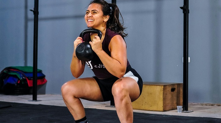 Lifter performing kettlebell goblet squat at full depth in a gym setting